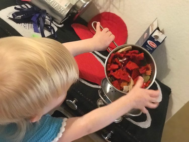 Back view of Zoey tilting the pasta and tomato mixture into a strainer on the stovetop. The red burner covers are laid out on the burner beside the pot and there's two more behind it.