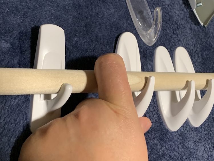 My finger holding the dowel in place on four medium sized command hooks.