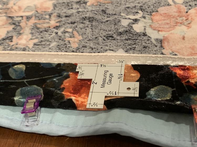 The top of the fabric is folded over and clipped in place. A measuring gauge is laid overtop so you can see that it's two inches from the fold to the selvage edge.