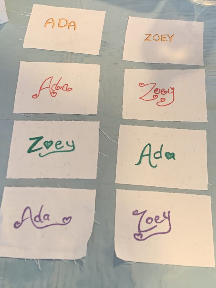 The white rectangles are laid out two across and four down. The first column contains squares with Ada's name on it while the second column contains Zoey's name. Each row is made with a  different color and font starting with orange and shadowing (top), then red, green, and finally (at the bottom) purple. 
