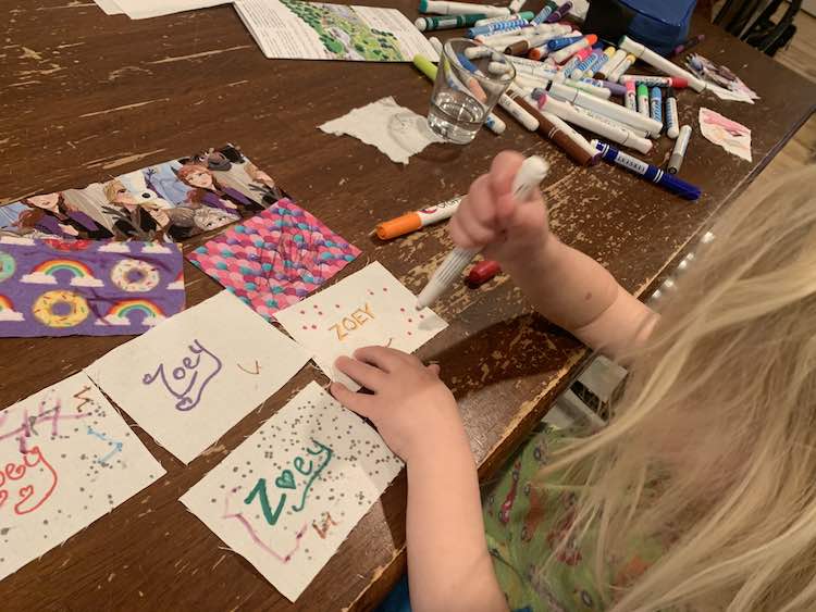 Foreground shows Zoey looking down while holding a fabric marker and dotting the square below her. All her squares are laid out around it. In the background are the rest of the fabric markers and Ada's area.