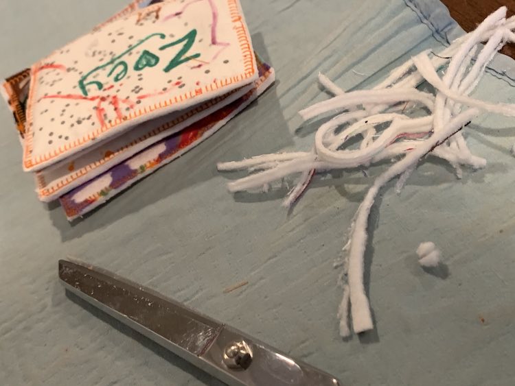 Foreground shows a part of my scissors while the pile of finished name tags sit in the background. The trimmed fabric lays between the two off to the right. 