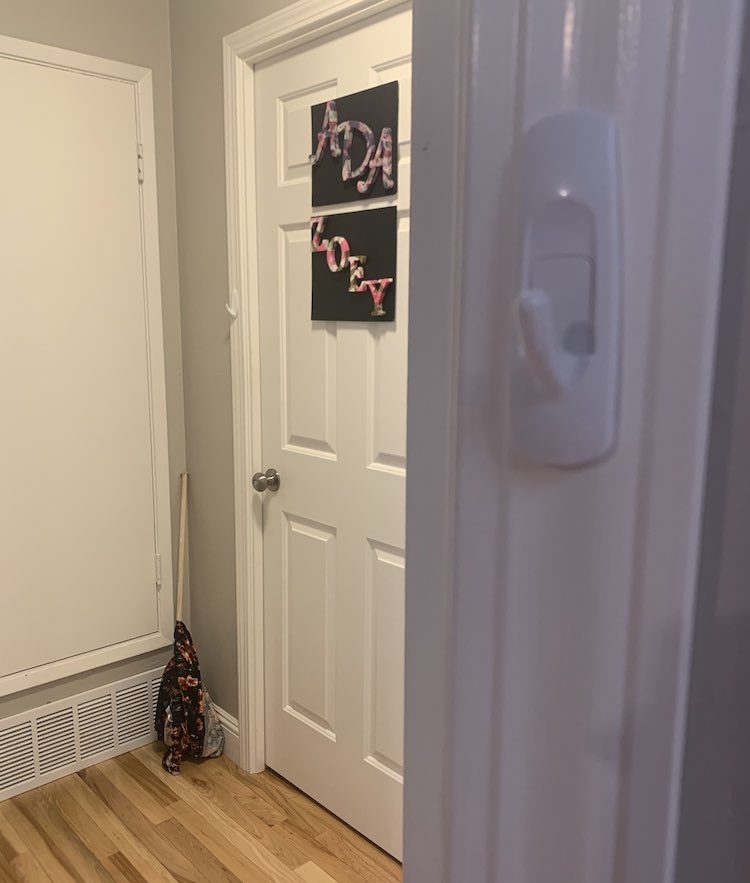 The center left side of the image shows the dowel on it's end with the curtain wrapped around it leaning in the corner. The bedroom door is closed and you can see one of it's command hooks sitting on the door frame. In the slightly unfocused foreground, to the right, you can see a closeup of one of the living room doorway's command hooks. 