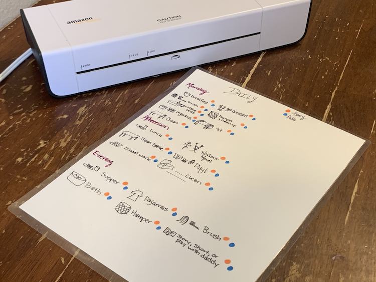 Closeup view of our first schedule with the laminator in the background. The day was divided into morning, afternoon, and evening. Each item on the list was accompanied with an orange and blue dot so each kid could scribble out the dot when that item is done. That paper is laminated so I could wipe it clean each night.