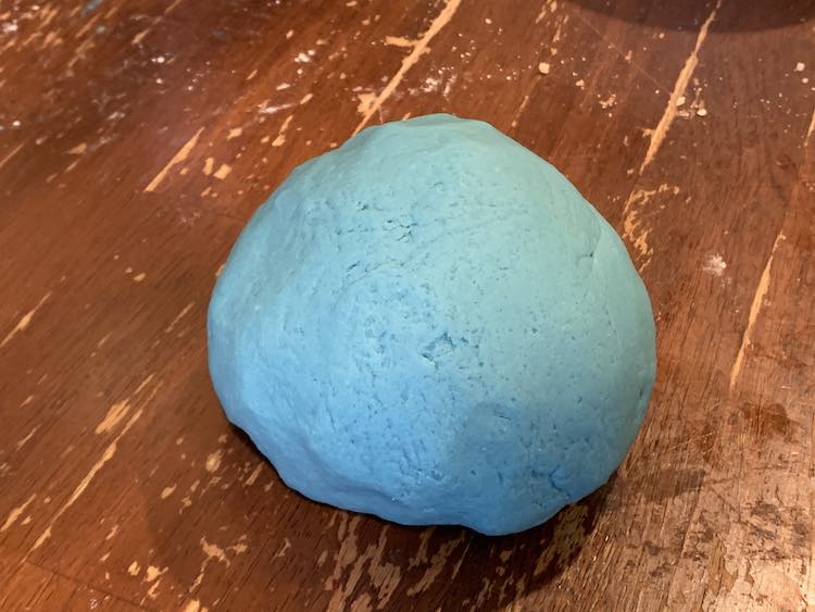 A smooth ball of blue playdough resting on the table. 