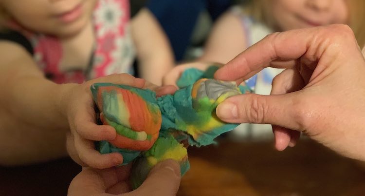 Image shows five hands holding up their somewhat triangular cake pieces. The cake and hands closer to the camera are in focus while the background is blurred.