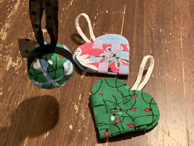 Image is a simple photo showing two weaved heart ornaments laying on a table with a spherical ornaments on black bias tape held up above and to the side of them.