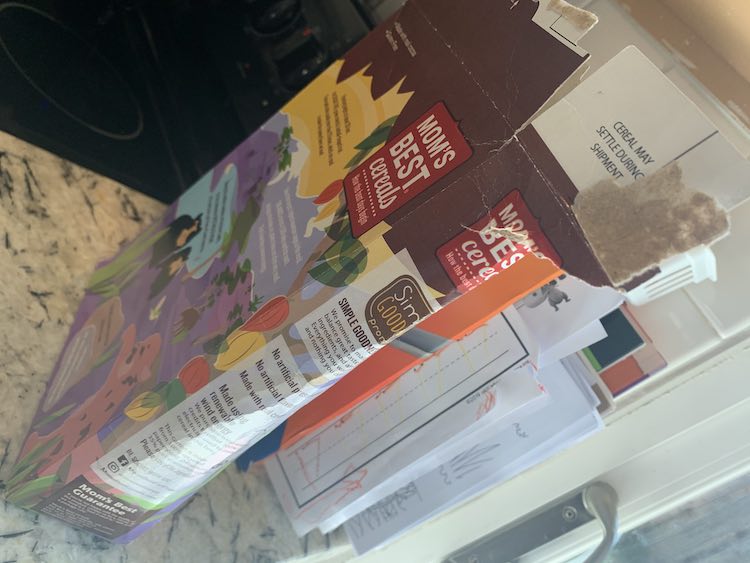 The small, bent, rounded, and ripped cereal box barely stands on it's own on the counter. Behind it, barely seen, is the newer, larger, and strong paper organizer box.
