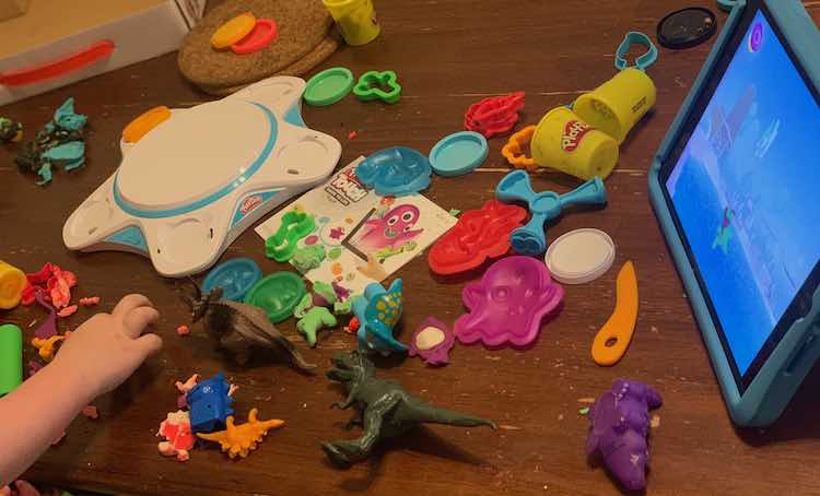 Image shows the kitchen table spread out with plastic dinosaurs and the Play-Doh kit. The iPad shows the playdough creation just as well as the old Play-Doh one.