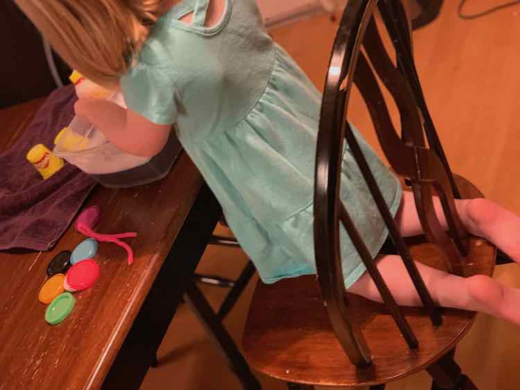 Ada on her knees on a chair leaned over a bin of soapy water cleaning the containers. 