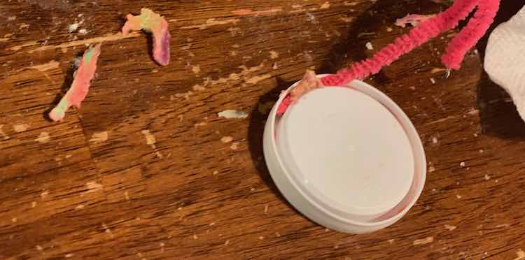 Image shows a closeup of the pink pipe cleaner pushing the Play-Doh gunk out of the lid's grooves. 