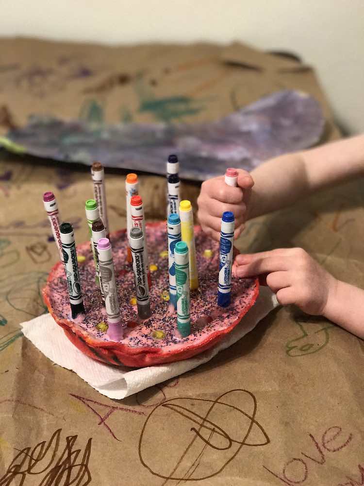 Clseup of Ada pulling out a pink marker from the felt pen holder. The holder sits on a piece of paper towel on a brown paper lined table. A painted paper stocking sits in the background.