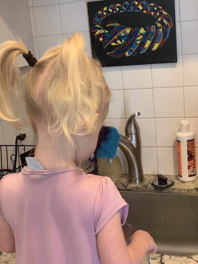 Back view of Zoey in front of our kitchen sink about to turn on the water and refill the measuring jug. 