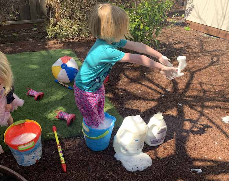 Mostly off screen to the left you see Zoey pulling up her dress looking like she's about to get into her red pail of soapy water. In the center if the photo Ada stands in her blue bucket filled with soapy water and throws a handful to the right. 