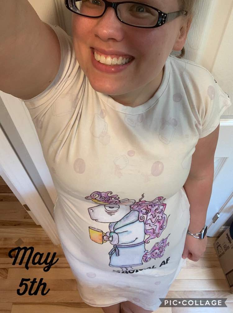 Selfie image of me looking up into the camera. I'm wearing a knee length, crewneck, short sleeved dress with a tired looking unicorn on it. The background of the fabric is faded, so the unicorn pops, with coffee beans, mugs, and spilled coffee. Slightly hidden, under the unicorn, it reads 'Still Magical AF'. To the left of me, at the bottom, there's black font saying 'May 5th'.