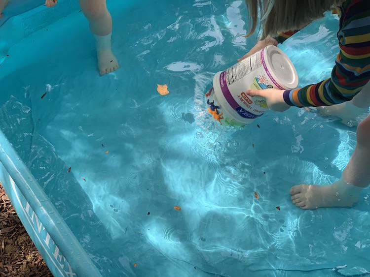 Zoey's foot off to the side shows her getting into the pool. To the right Ada is crouched over holding the upside down container dropping the ice into the pool. 