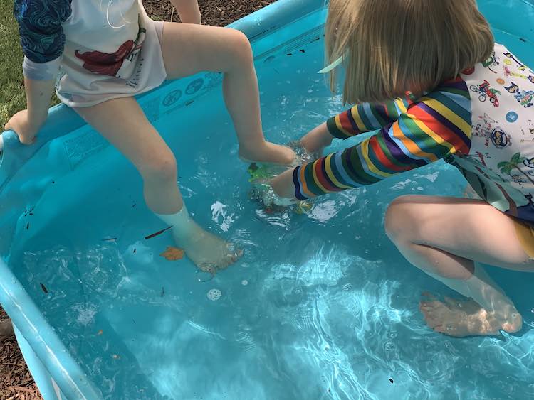 Zoey sitting on the edge with a foot on the ice underwater. Ada crouches next to it with both hands on the ice.