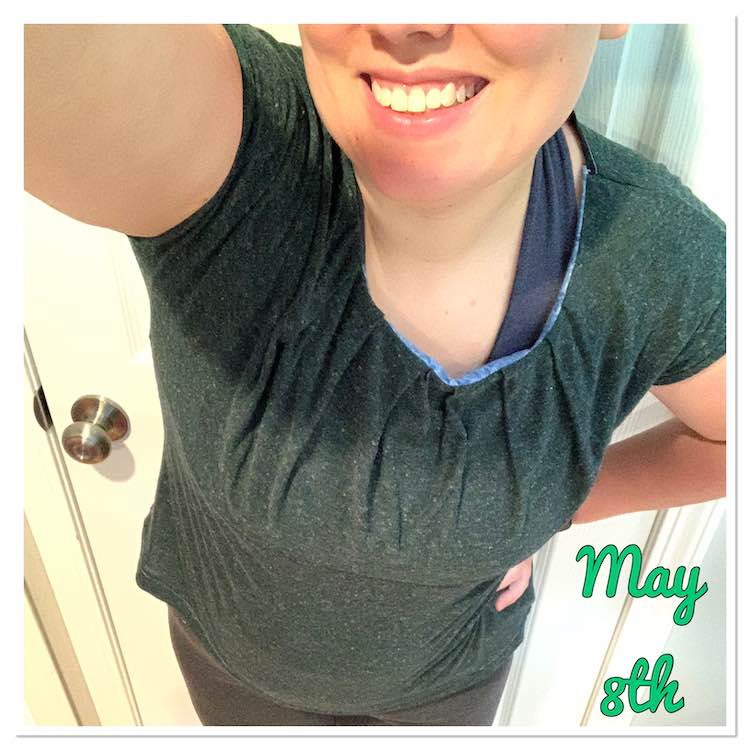 Selfie view of the bottom of my fave and shirt. The shirt is a green and white mottled fabric with pleats along the neckline. The blue woven fabric used as a lining is showing along that neckline too. Under the shirt you can see one of the straps of my blue brazi and my grey capris. Beside me, in green font, it says 'May 8th'.