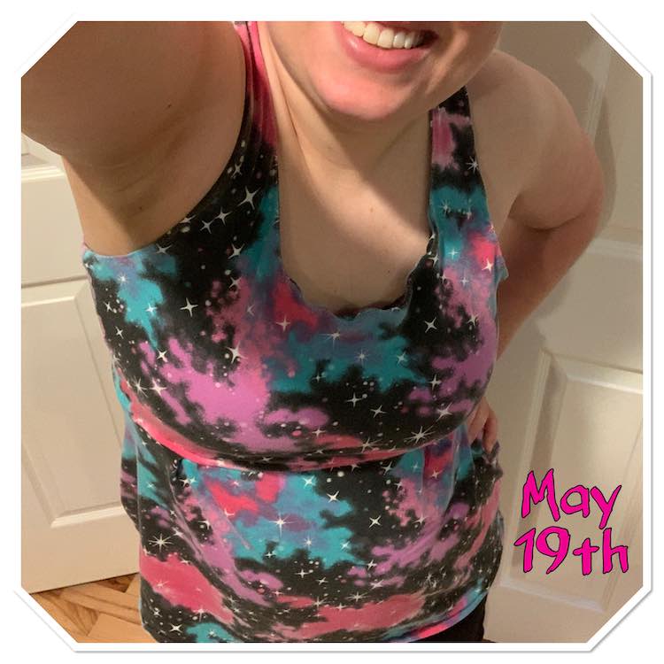 Selfie view of my top with the bottom bit cut off. The top is a sleeveless galaxy print shirt with a stretched out neckline and is brought in slightly under my breast. To the right of me are hot pink letters saying 'May 19th'.