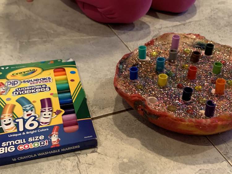 Photo shows a new package of Crayola Pop-squeaks skinnies markers, the emptied felt pen holder, and Zoey's pink clad knees.