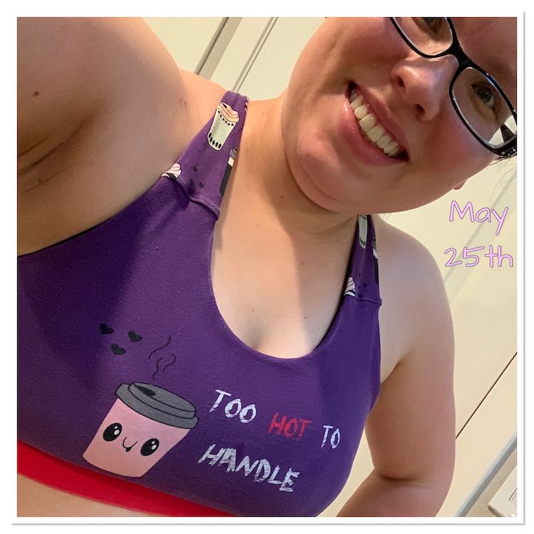 Closeup selfie showing most of my face and my workout bra. The bra is purple with a bright pink band underneath. Across my breast it has an adorable lidded cup and says 'too hot to handle'. The back, not seen, of the bra and top of the straps has small cups. 