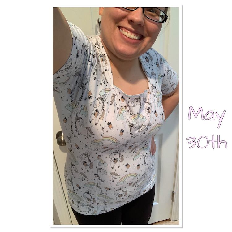 Selfie view showing a single eye down to the bottom of my shirt. The shirt is white with many rainbows, coffee cups, small hearts, and unicorns on it. If you look closely you can see the seam lines vertically over my stomach and showing the bra cups have been sewn together.