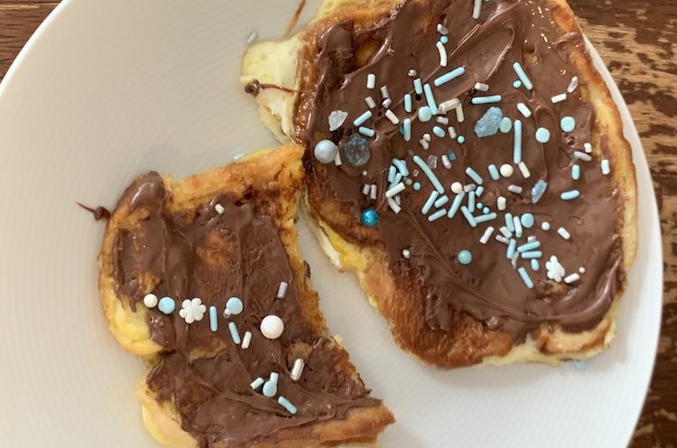 Overview of white plate with one and a half french toast slices decorated in brown Nutella and colorful blue and white 'ice' sprinkles from Walmart.