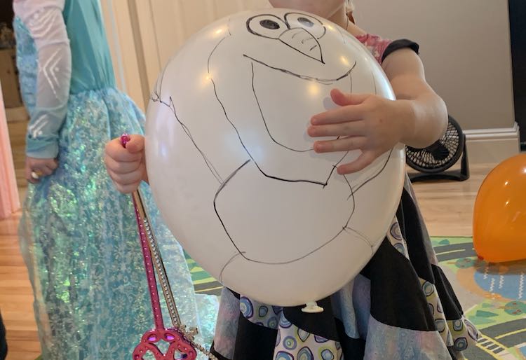 Closeup of the Olaf balloon in Zoey's arms, while she holds two wands, with Ada wearing an Elsa dress behind her.
