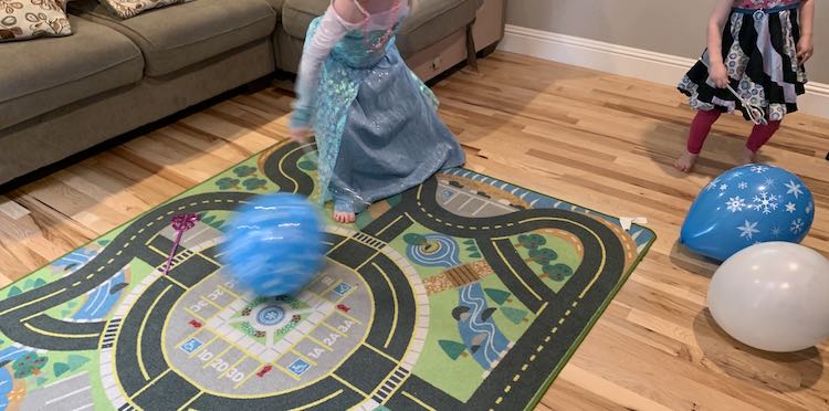 View of our living room floor during the party. Zoey is off to the side, behind two balloons, holding her wand. Ada is in the middle of the photo with her wand swung and the snowflake balloon in front of her moving away.