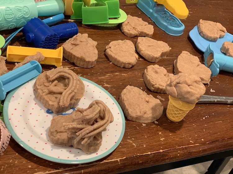 Image shows a table coated in heart cookies, Play-Doh tools, a plate of decorated cookies, and a single ice cream cone.... all brown and cinnamon scented.