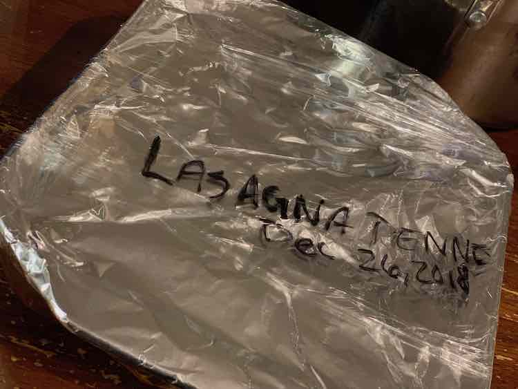 View from above with the casserole dish top wrapped in tinfoil and then, partially, with plastic wrap. On the top of the plastic wrap it was written, in black, "LASAGNA PENNE/Dec 26, 2018".