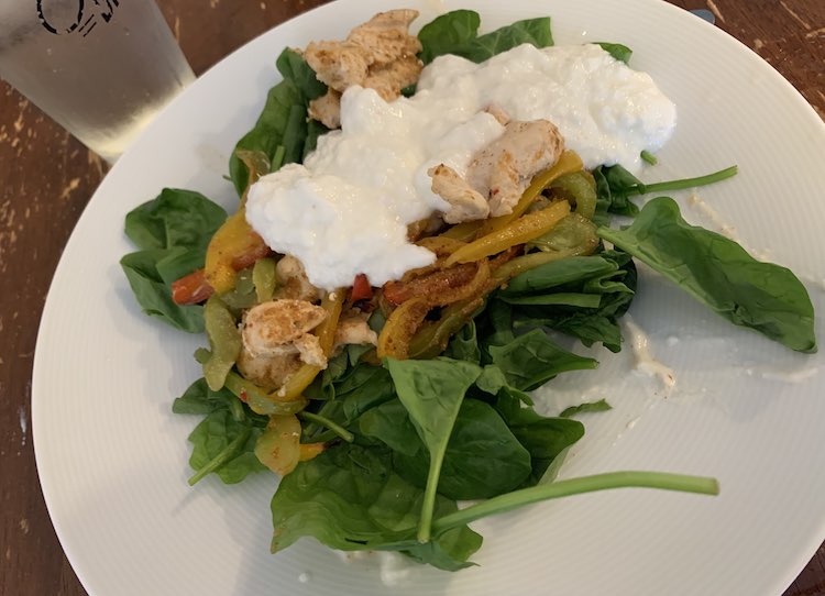 Closeup of a white bowl containing spinach leaves, chicken fajita mix, and plain white yogurt.