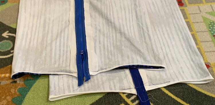 Both pillows are shown, stacked, with the zipper facing up. If you look at the fabric on either side of the zipper, at the bottom, you can see the blue thread showing where the zipper was sewn down.
