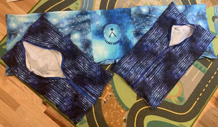 The photo shows the long Stargate pillow (center panel with coordinating fabric to the left and right) laid over the car mat on our living room floor. Overtop of the pillow, angled away, lay two matching navy striped matching pillows both with a blue (mismatched) zipper along the center length of them halfway opened.