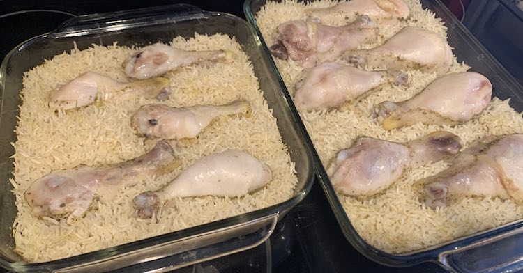 Angled overview looking down at the square (left) and rectangular (right) casserole dishes filled with cooked and seasoned rice topped with baked chicken drumsticks. 