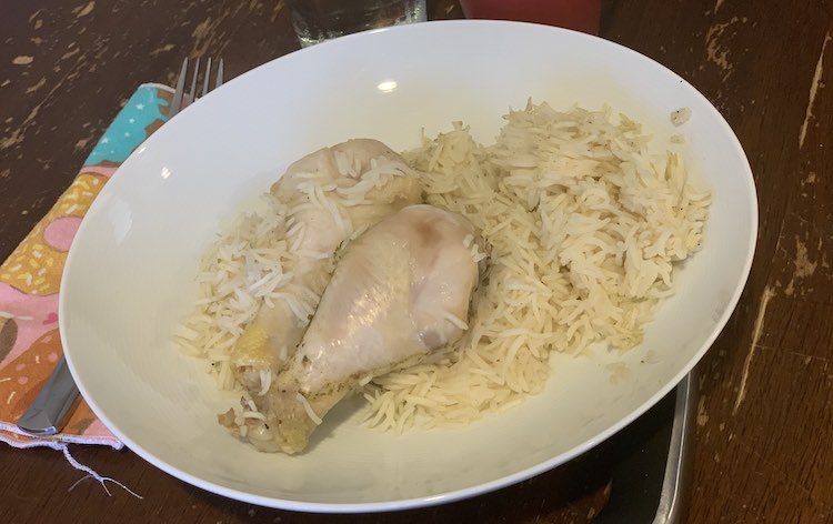 View looking down at a large white bowl with rice and two drumsticks. 