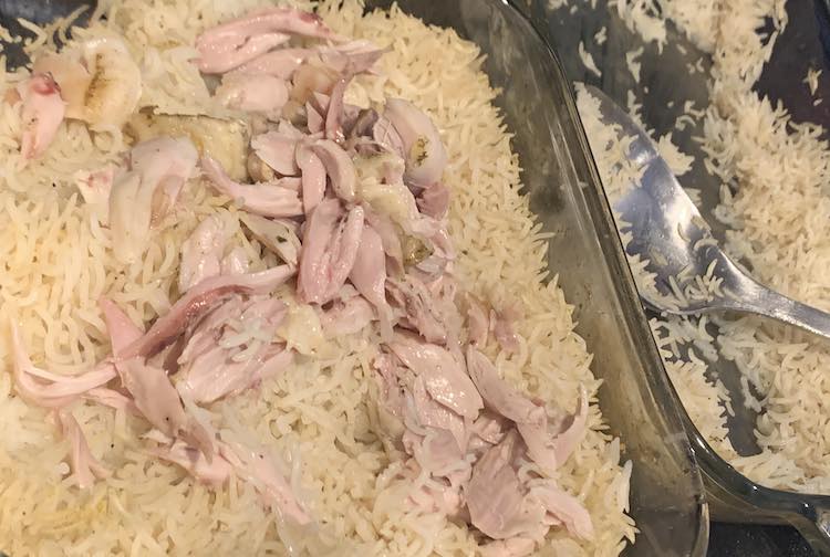 Closeup of the square casserole dish filled with rice and broken up pieces of chicken. To the right is the other casserole dish with a metal serving spoon and rice. 