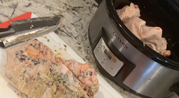 View of the Crockpot, to the right, with chunks of frozen stew in it. To the left is the cutting board with the two knives off to the side and a large chunk of stew with a groove down the center of it.