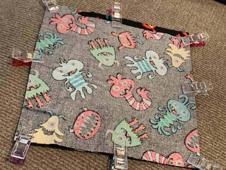 The wrong side of the fabric is shown, with a scrap of the right side of the fabric showing through the top from the fabric below, and is clipped on all four sides to keep the two pieces together.
