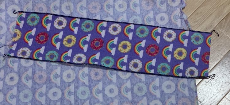 The long rectangle of 'napkin' is shown with the long edges sewn down and the top and bottom unsewn. It lays on the rest of the fabric it was cut from.