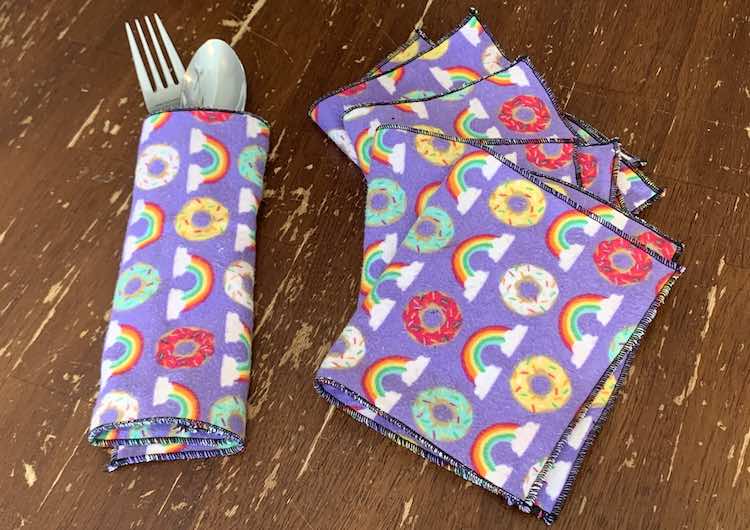 The photo shows a fork and spoon wrapped up in a napkin, on it's side, on the left of the photo. The right side of the photo shows the other four napkins folded in half and slightly overlapped making a slight arch going up the photo.