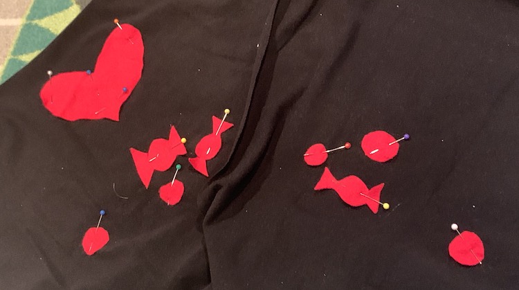 Image shows a section of the front and back shirt pieces highlighting the red flannel heart, candy, and circular pieces pinned to the black knit fabric. 