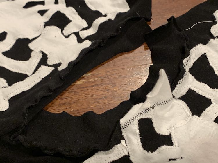 Image shows the opened neckline with the binding sewn on, right side to wrong side, so there's black thread zigzagging over the white bones. 