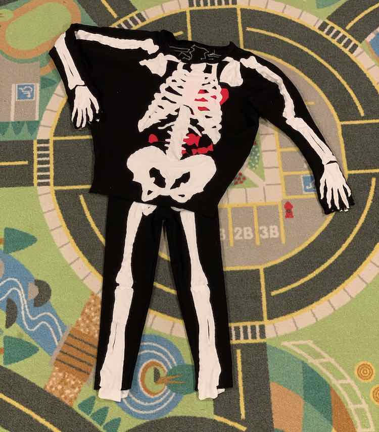 Image shows the pants, with an unhemmed bottom, and shirt laid out on the car mat. The shirt overlaps with the top of the pants so there is only one pelvis. Through the neckline you can see the inside back of the shirt showing the bone's outlines. 