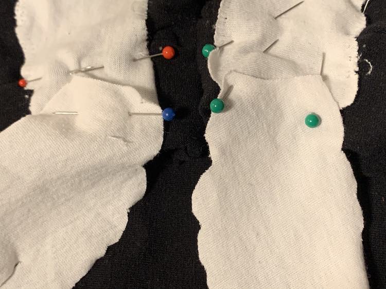Image shows a closeup of the bottom part of the pants along the pant cuff. The bottom of the leg bone is overlapping the seam on the cuff and is pinned over top. Above it sits the top of the foot bone. It is also pinned in place. 