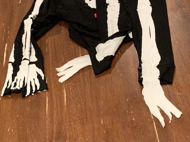 Image shows a closeup of the skeleton's hands and feet. The two sleeves are draped down from the top of the image on the left while the two feet drape down on the right. The one pant leg is folded up so you can see the backside and how the foot is only sewn on the front side. 