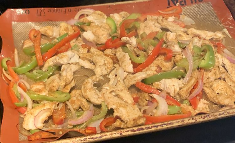 Closeup of the sheet pan showing baked white chicken, sliced red peppers, sliced green peppers, and sliced onion.