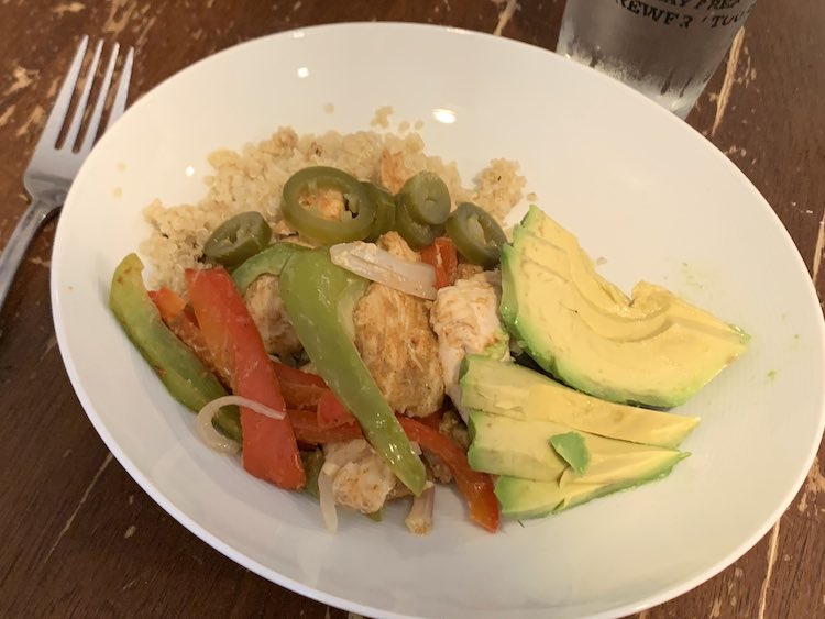 Closeup of a white plate containing quinoa, chicken fajitas, sliced jalapenos, and sliced avocado.