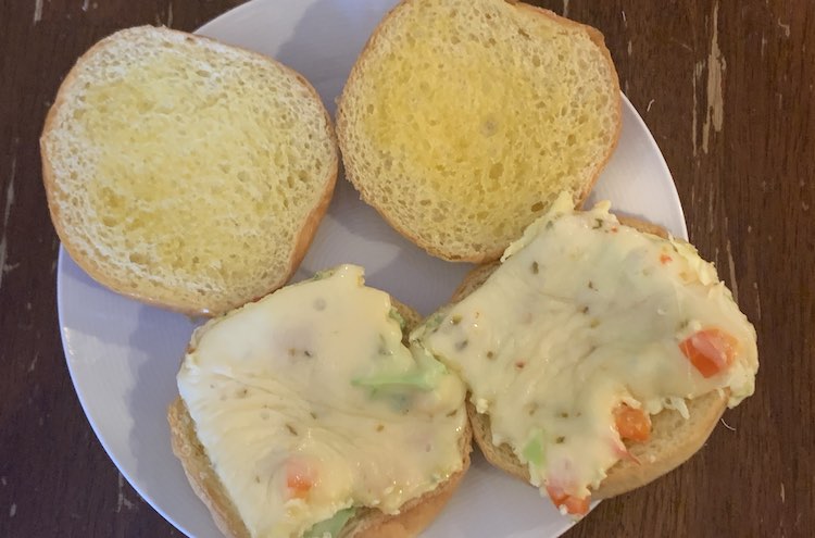 Closeup of two buns, opened, on a white saucer. There is a square of pepper jack cheese covered eggs on the bottom buns and the top buns are clearly buttered and toasted.