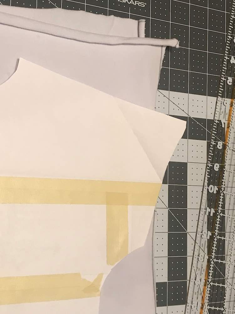 Overview showing the folded white panel with the paper pattern laying overtop of it. The top of the sleeve is jutting out over the fabric and doesn't fit. The background of the image shows a cutting mat and ruler. 